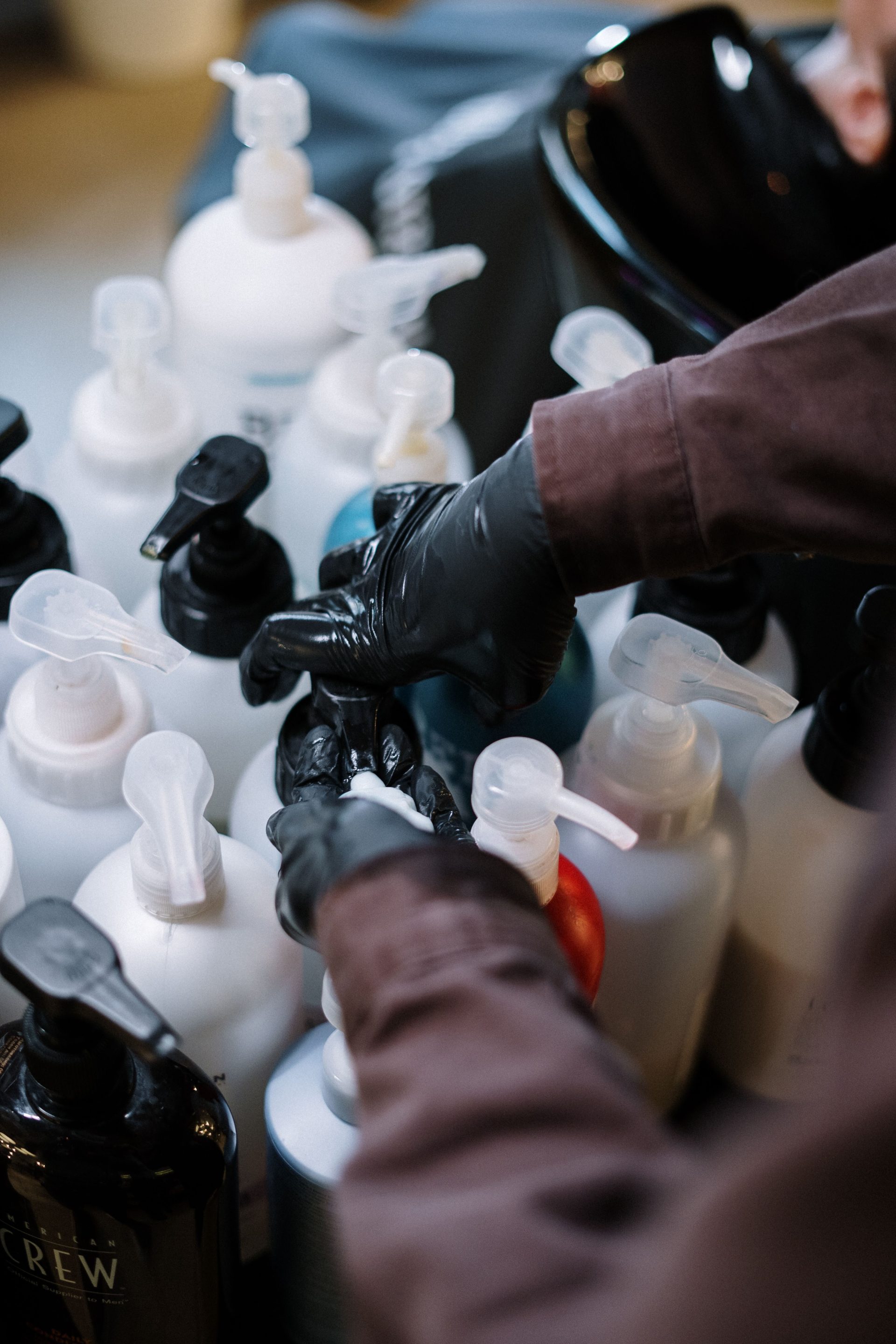 A hairdresser with gloves arranges hair care products in a salon setting.